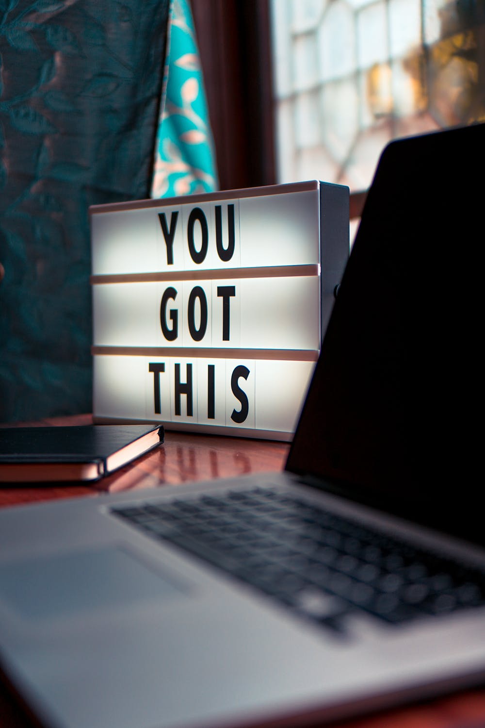 "A lightbox with the message "YOU GOT THIS" placed on a desk next to a laptop and a notebook, promoting motivation and productivity."