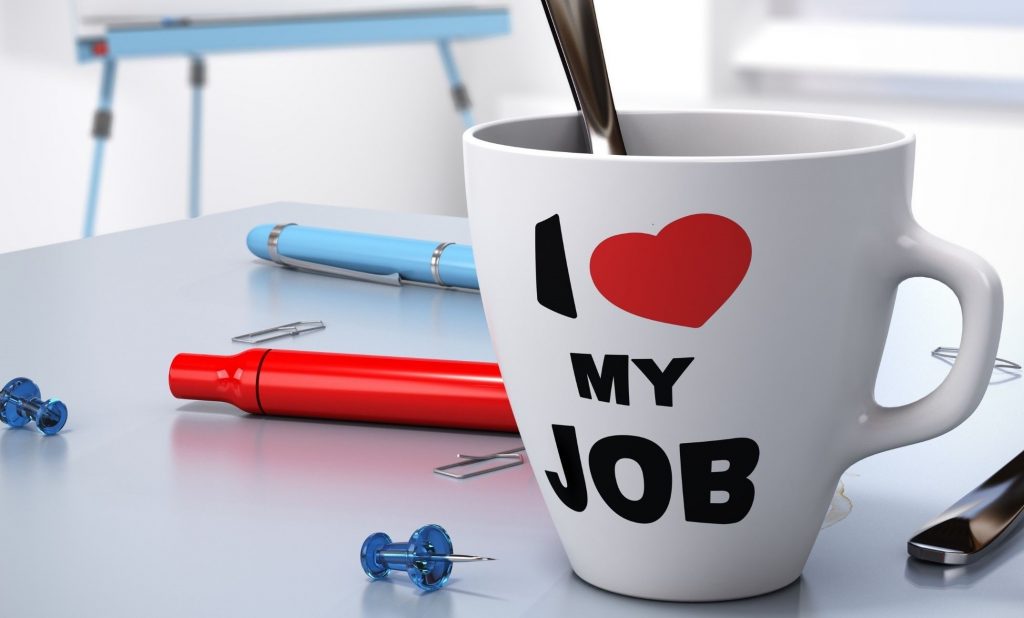 "White coffee mug with "I ❤️ MY JOB" printed on it, placed on an office desk with pens, pushpins, and paperclips."