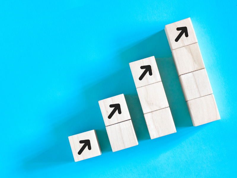 Wooden blocks stacked in increasing height with upward arrows, representing business growth, success, and positive progress.